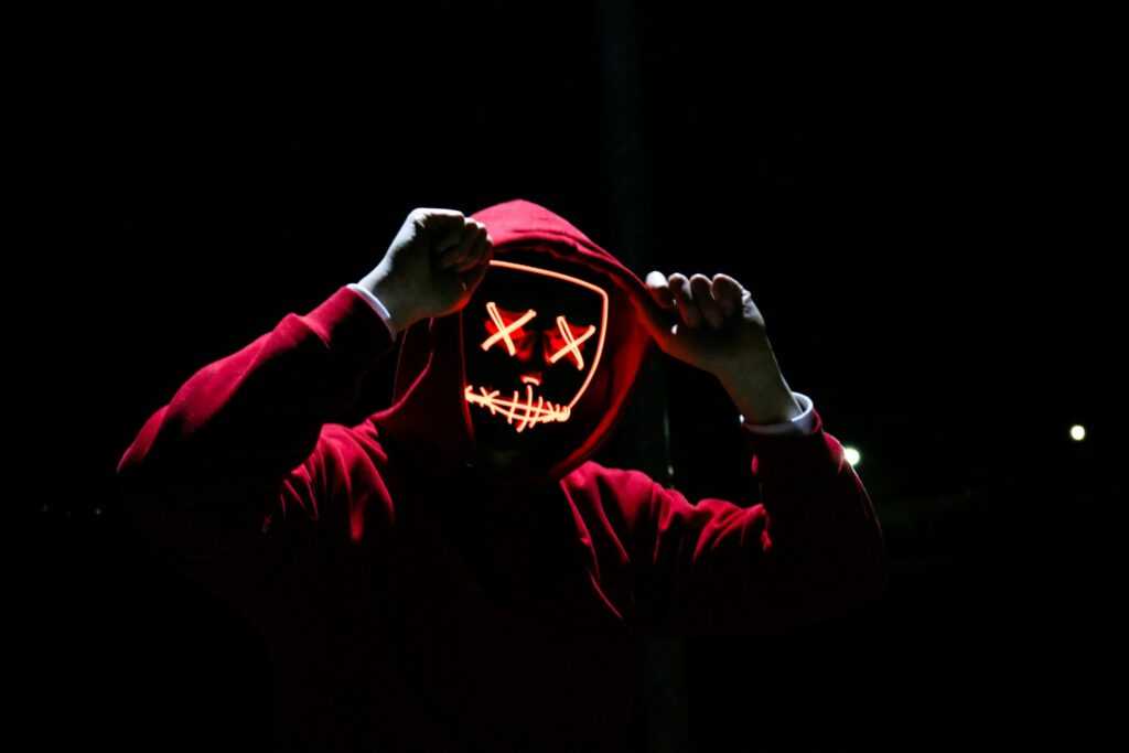 pexels photo 1097456 1097456 A spooky illuminated mask figure with a red hoodie in a dark setting, perfect for Halloween themes.